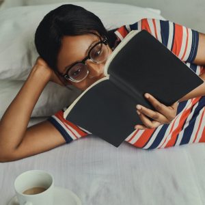 A Woman Lying in Bed with a Cup of Coffee and Reading a Book