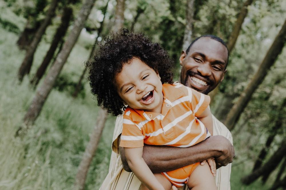 A Laughing Man Holding a Visibly Ecstatic Child to His Chest in a Woody Setting